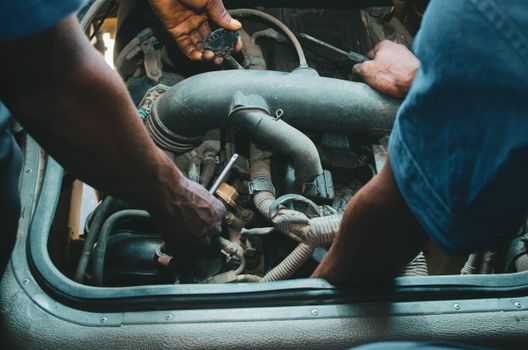 Auto mechanics repairing an engine in a Nigerian workshop. Close-up hands and tools.